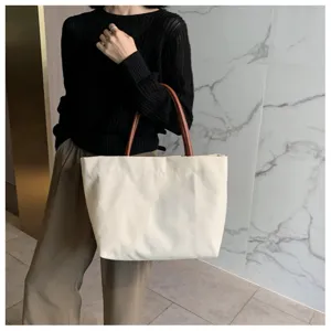 Vue détaillée d'un sac cabas minimaliste en toile blanche avec anses marron pour le quotidien.