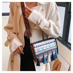 Detail shot of ethnic embroidered crossbody bag with wide patterned strap and chic colorful tassels.