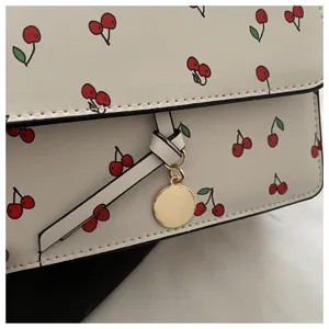 Gros plan détaillé d'un sac bandoulière blanc crème avec imprimé cerise rouge.