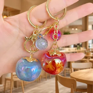 Acrylic persimmon keychain close-up, cute fruit bag charm detail, gold tone hardware accessory.