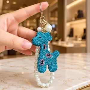 Close-up of cute blue rhinestone giraffe keychain with elegant pearl bracelet strap detail.