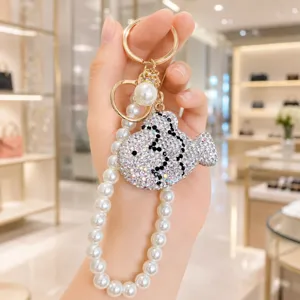 Rhinestone crystal fish keychain detail with elegant pearl strap and golden hardware shine.