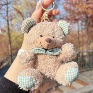 Close-up of a cute fluffy teddy bear plush keychain with green checkered bow and details.