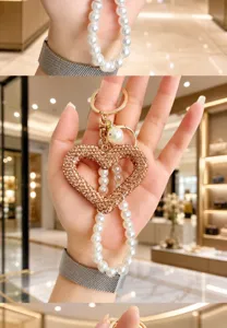 Close-up detail shot of the elegant rhinestone heart keychain with pearl strap and gold hardware.