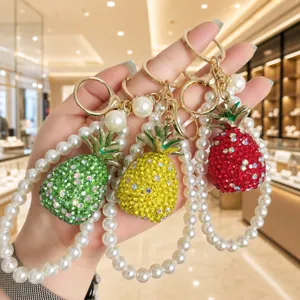 Close-up of sparkling rhinestone pineapple keychain with elegant faux pearl strap for bags.