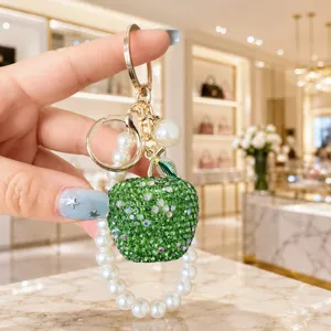 Detail view of the luxury green crystal apple keychain with elegant pearl bracelet.