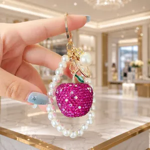 Detailed close-up of the dazzling rhinestone apple pendant and pearl wrist strap keychain charm.