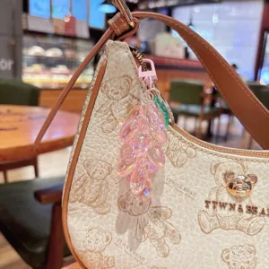 Vista detallada del bolso con diseño de osito y colgante de racimo de uvas de acrílico rosa.