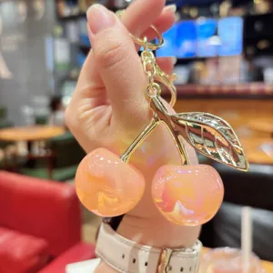 Close-up detail of glossy pink resin cherry bag charm, shiny gold metal stem hardware.