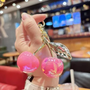 Charming pink resin cherry keychain detail, elegant gold metal stem and leaf pendant.