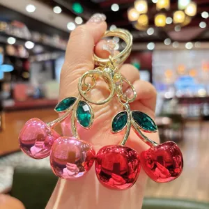 Close-up view of shiny electroplated cherry keychain with green rhinestone leaves and bag charm.