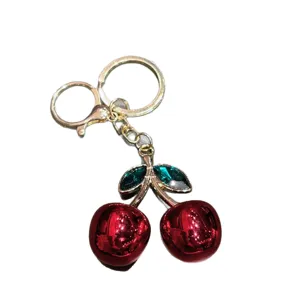 Cute red cherry keychain with gold hardware and sparkling green crystal leaves for bags.