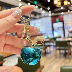 Primo piano dettagliato di portachiavi a mela in cristallo blu con stelo dorato, accessorio.