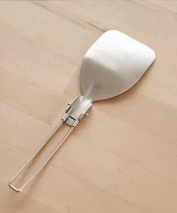 Stainless steel folding spatula detail, compact camping cookware surface closeup view for travel.