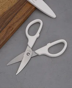 Closeup of white handle stainless steel kitchen scissors with protective cover and wooden board.
