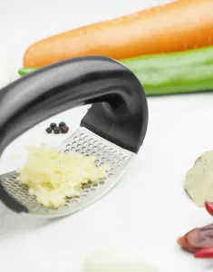 Detail shot of stainless steel rocking garlic press with minced garlic and spice props.