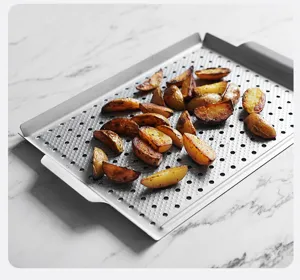 Stainless steel perforated square grill pan detail shot with roasted potatoes on marble table.