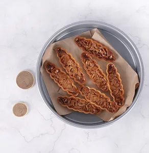 Round metal baking tray with almond pastries on parchment paper for kitchen baking use.