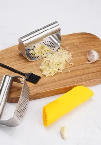 Detalle de prensa ajos de acero inoxidable con ajo machacado, tabla de madera y pelador.