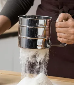 Tamis a farine en acier inoxydable detail avec filet fin et poignee pratique pour patisserie.