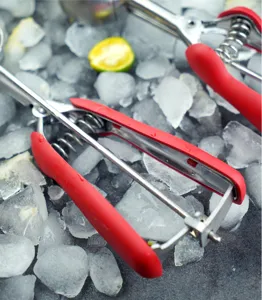 Stainless steel ice cream scoop with red silicone handle detail on crushed ice.