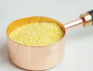 Gros plan détaillé d'une tasse à mesurer en or rose remplie de mil, texture métallique.