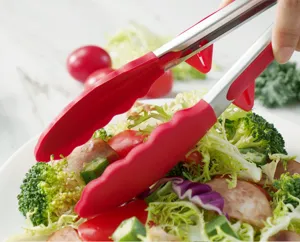 Detailaufnahme einer EdelstahLZange mit rotem Silikonkopf beim Greifen von frischem Salat.