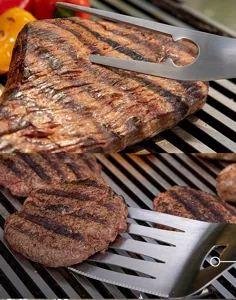 Stainless steel BBQ tool detail, grill spatula and fork in action, outdoor cooking gear.