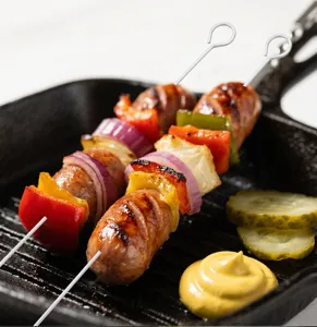 Dettaglio di spiedini da barbecue in acciaio inox con impugnatura ad anello e salsiccia.