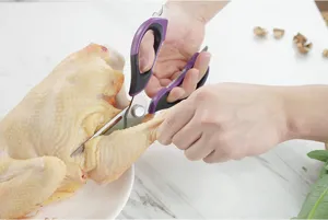 Ciseaux de cuisine démontables en action, coupant du poulet cru sur un plan de travail.
