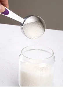 Stainless steel measuring spoon detail showing 60ml capacity and sugar pouring into glass jar.