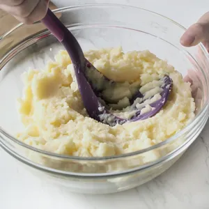 Presse-purée de cuisine avec manche violet pour préparer une purée de pommes de terre lisse.