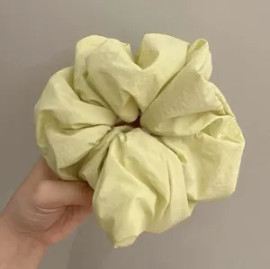 Detailed view of a light yellow fluffy hair scrunchie, showcasing its soft fabric and soft volume.