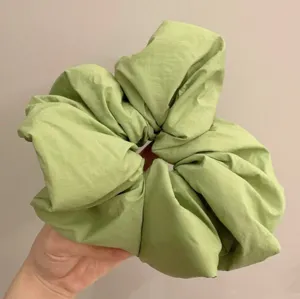 Large green scrunchie detail view, fluffy fabric hair tie for stylish everyday hairstyles.