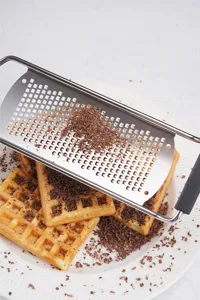 Edelstahler Käsereibe und Schokoreibe Detailansicht zeigt feine Schokoraspeln auf Waffeln.