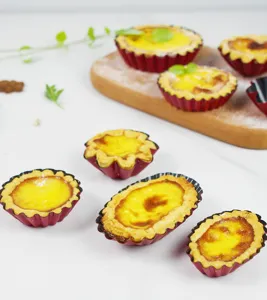 Detailed shot of red fluted baking tart molds with freshly baked egg tarts on wooden board.