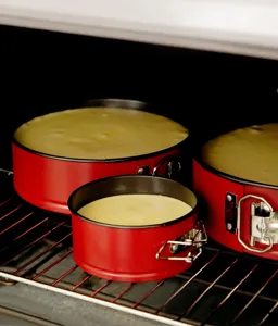 Close-up detail of red round springform cake pans set baking inside kitchen oven.