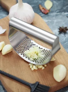 Stainless steel garlic press detail showing curved mesh and minced garlic on cutting board.