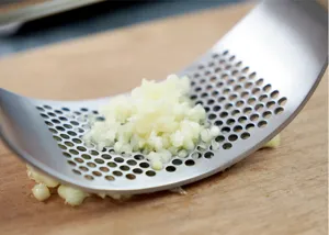 Close up detail of stainless steel garlic press on wooden cutting board with minced garlic.