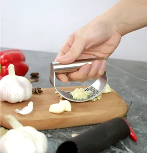 Stainless steel garlic press detail showing hand pressing garlic on wooden cutting board.