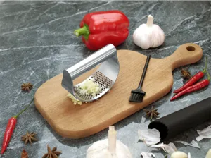 Stainless steel garlic press detail shot showing the ergonomic rocking design and minced garlic.
