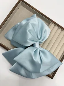 Detailed close-up of a large satin bow hair clip in ice blue, elegant design for styling.