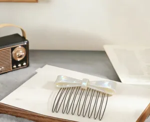 Nahaufnahme des eleganten weißen perlmuttartigen Schleifen-Haarkamms mit haltbaren Metallzähnen.