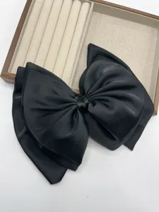 Close-up detail of the elegant black satin large bow hair clip, showing exquisite texture.