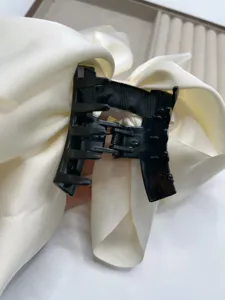 Elegant black claw clip with a large white satin bow for stylish everyday hair styling.