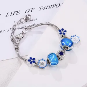 Gedetailleerde close-up van een zilverkleurige bedelarmband met blauwe emaillen bloemen.