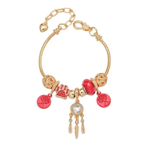 Close-up van gouden bedeltjesarmband met rode dromenvanger, pootafdruk en boomhanger.