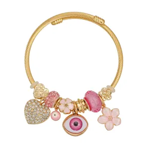 Dettaglio di un braccialetto con ciondoli dorati, malocchio rosa e cuori di strass.