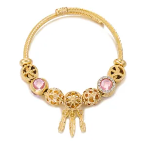 Close-up detail of the gold-plated cable wire charm bracelet with dreamcatcher and pink gems.
