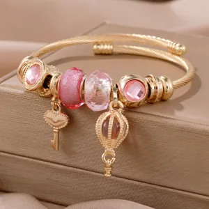Primer plano de una pulsera dorada con cristales rosas, dijes de llave corazón y globo.